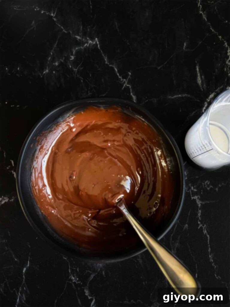 Lustrous, smooth chocolate ganache in a small dark bowl, ready to be drizzled over the bundt cake.