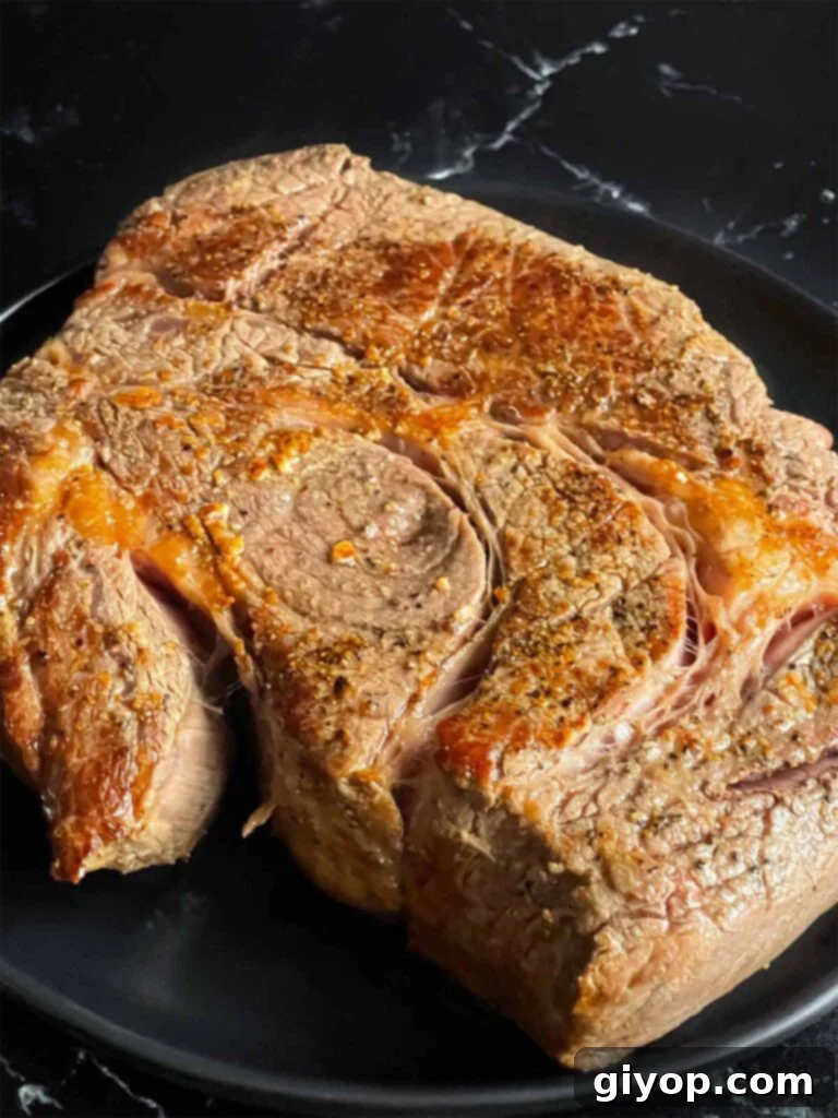 Seared chuck roast on a dark plate on a dark surface.