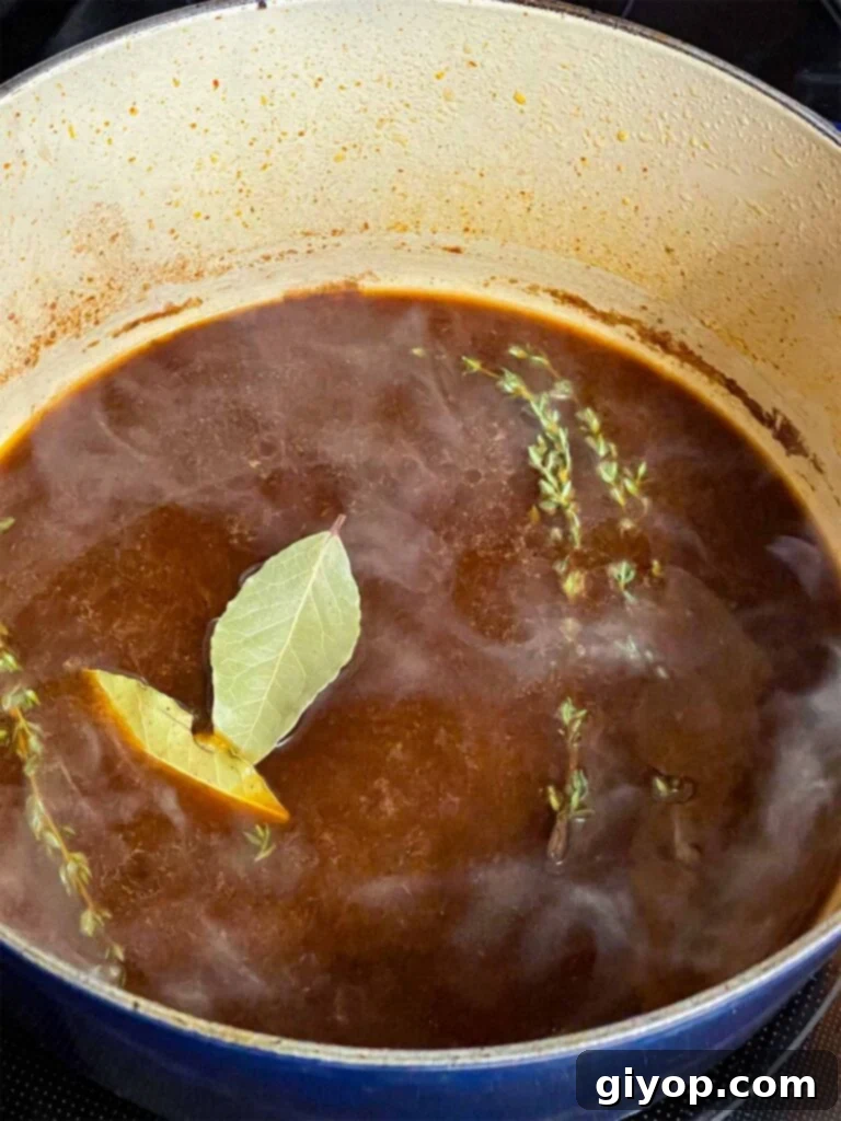 Beef broth, bay leaves, and fresh thyme added to a dutch oven for the pot roast recipe.