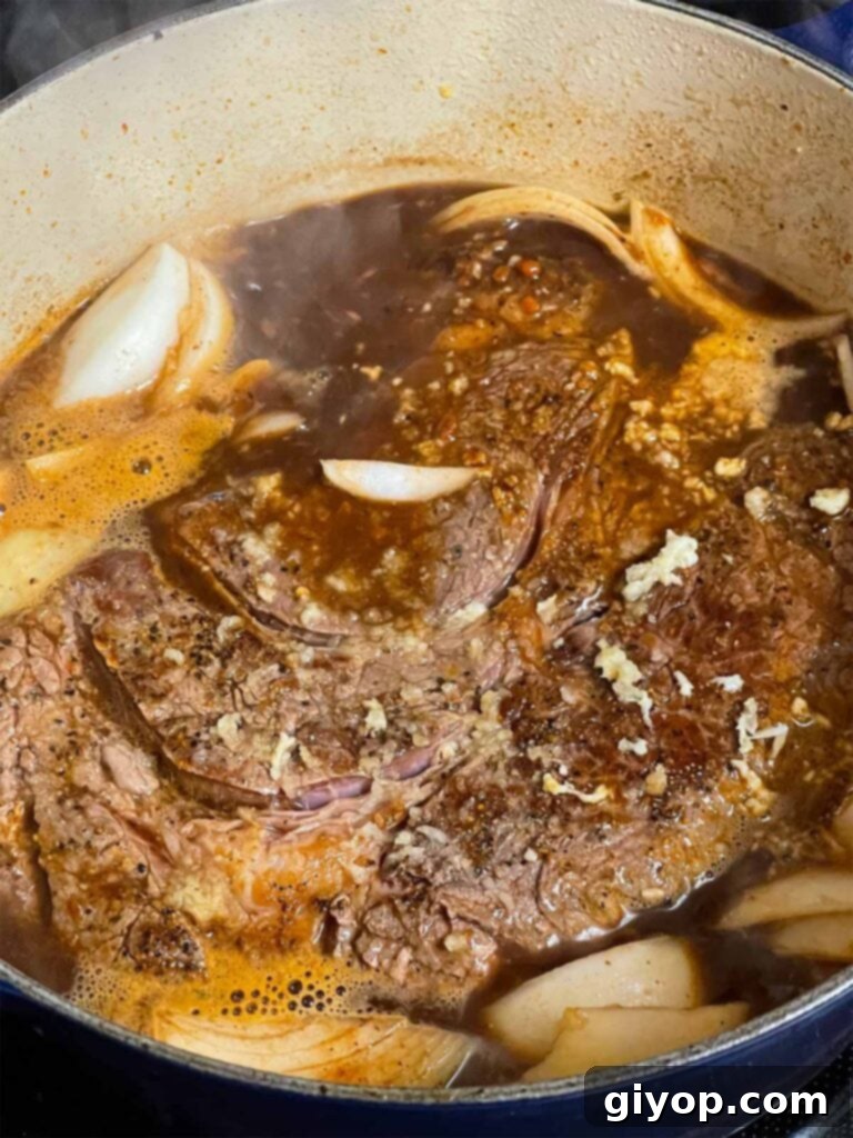 Chuck roast, onion, and garlic added to the beef broth in the dutch oven.