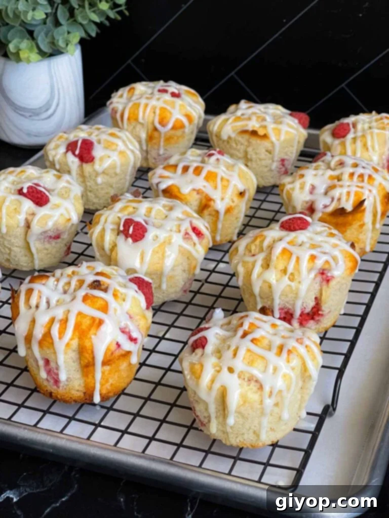 Freshly baked raspberry muffins, beautifully adorned with a zesty lemon glaze, cooling on a wire rack above a baking sheet lined with parchment paper, showcasing their bakery-style finish.