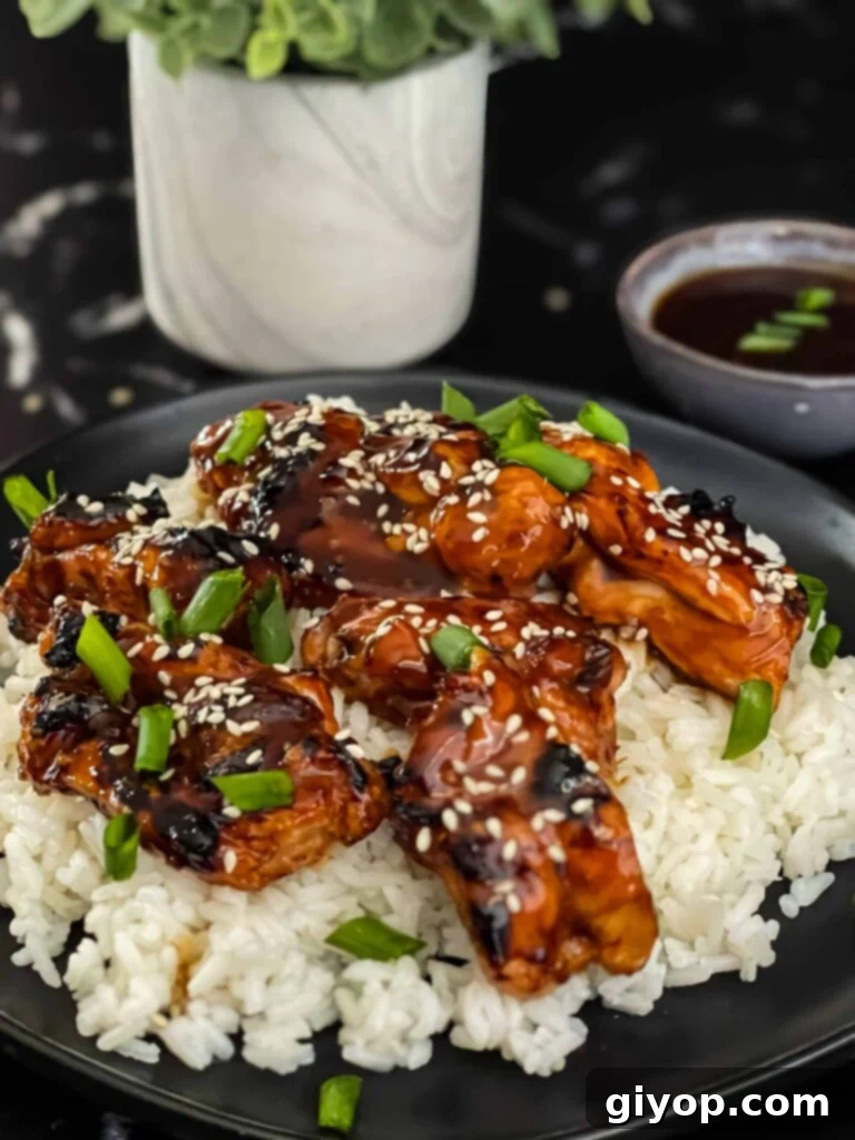 Bourbon chicken on a bed of white rice on a dark plate, garnished with sesame seeds and green onion.