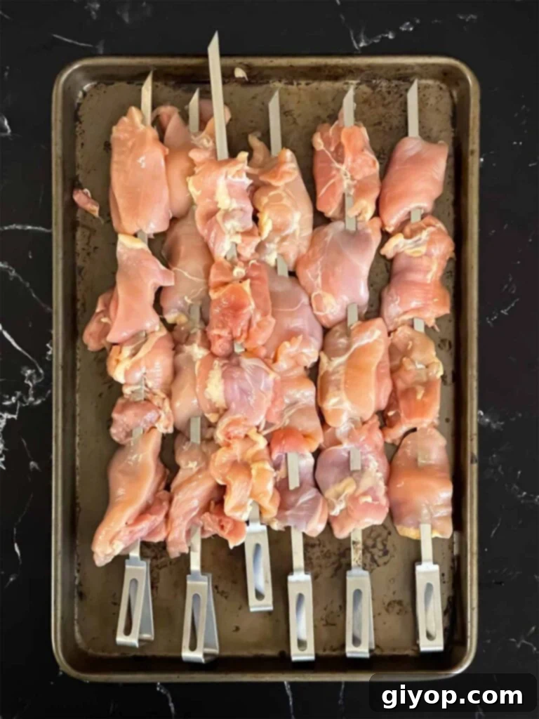 Raw chicken thighs, skewered, on a sheet pan.