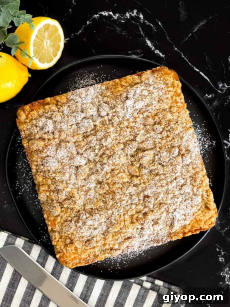 Baked lemon crumb cake dusted with powdered sugar on a dark plate on a dark surface.