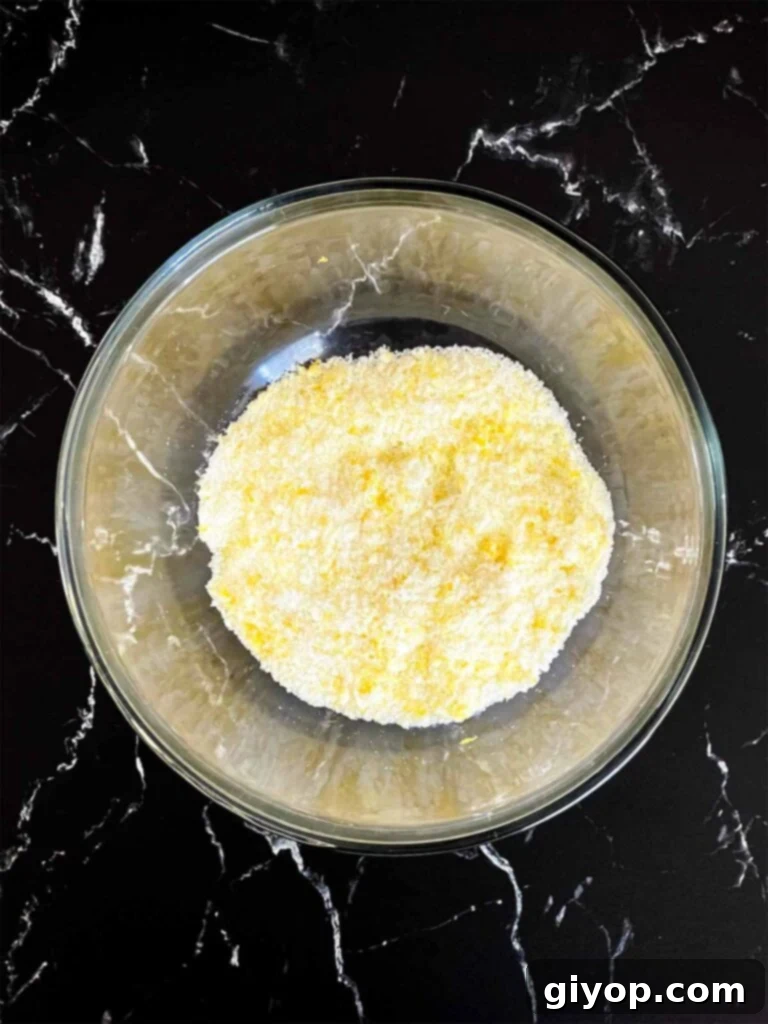 Lemon zest and granulated sugar rubbed together in a glass mixing bowl for lemon crumb cake recipe.