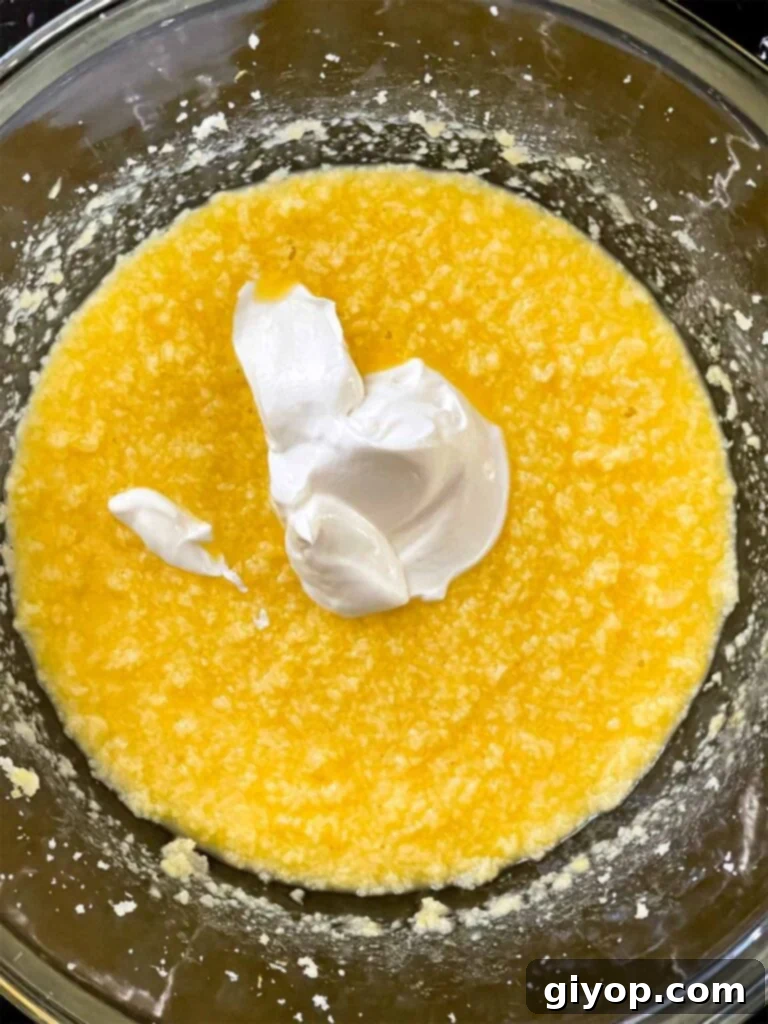 Sour cream added to the wet ingredients for lemon crumb cake in a glass mixing bowl.