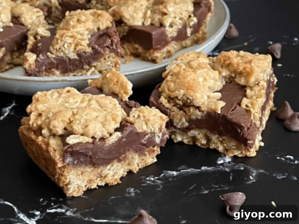 Chewy Oatmeal Fudge Bars 2 Delicious oatmeal fudge bars arranged on a dark serving surface, with a plate of additional bars in the background, showcasing their irresistible layers.