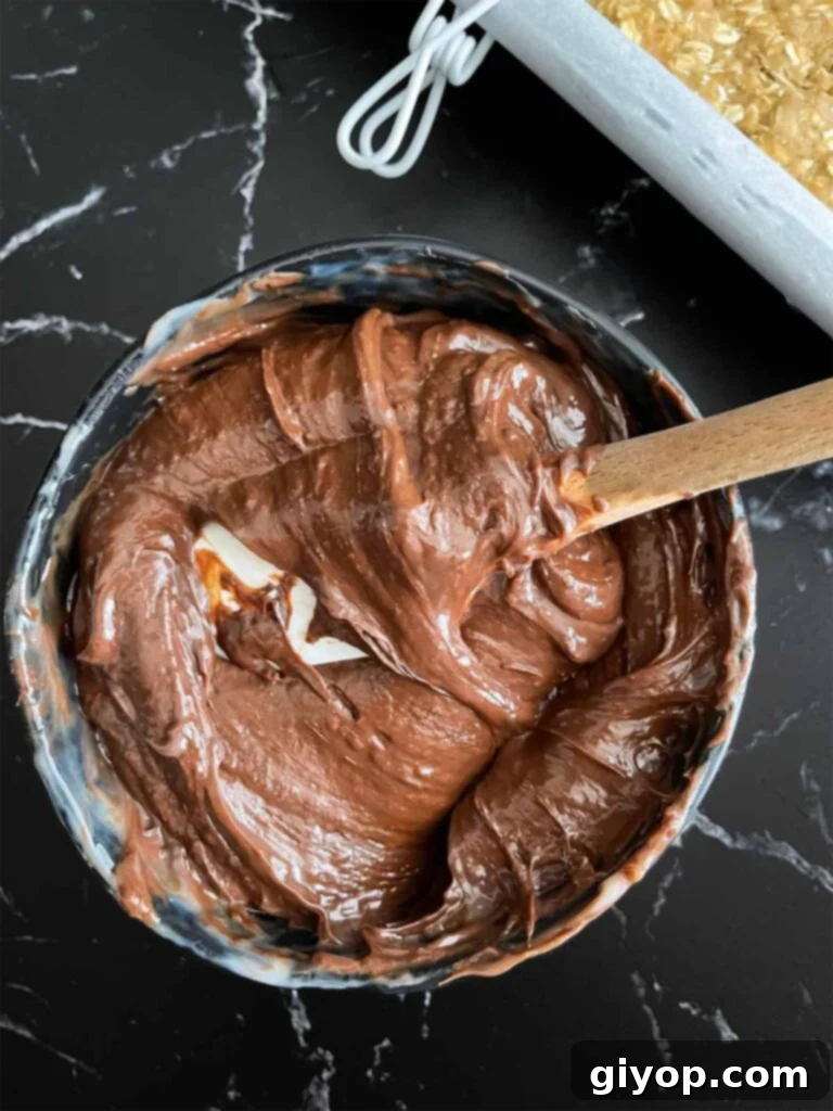 Chewy Oatmeal Fudge Bars 7 The smooth, glossy mixture of melted chocolate, condensed milk, and butter for the fudge layer, perfectly prepared in a dark bowl on a dark surface.