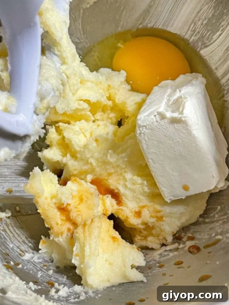 Cream cheese, a large egg, and vanilla extract are added to the creamy mixture of butter and lemon-infused sugar, ready to be beaten for the lemon thumbprint cookies.