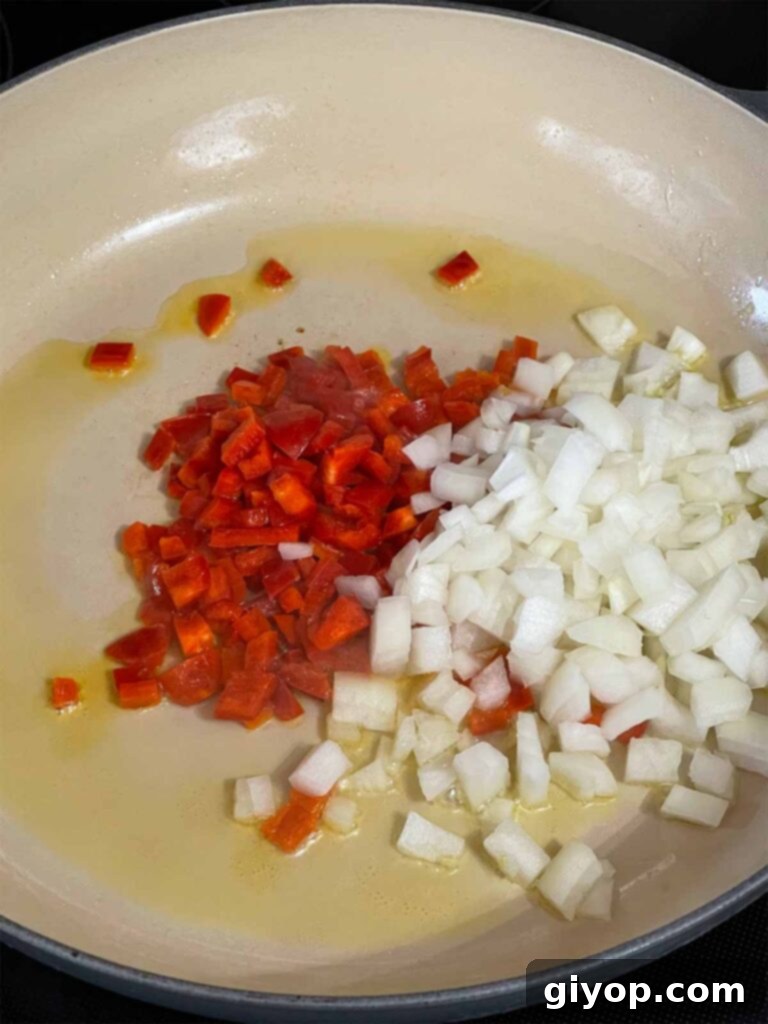 Diced onion and red bell pepper sautéing in a skillet.