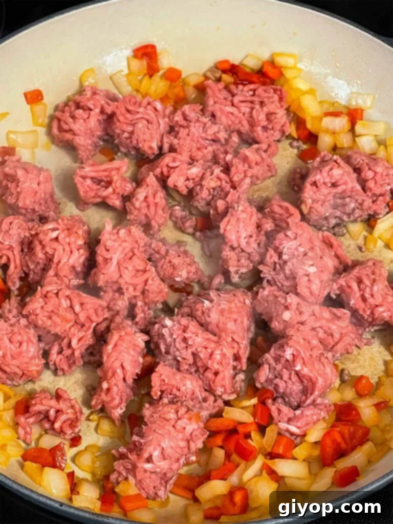 Ground beef added to sautéed onions and red bell pepper in a skillet, beginning to brown.