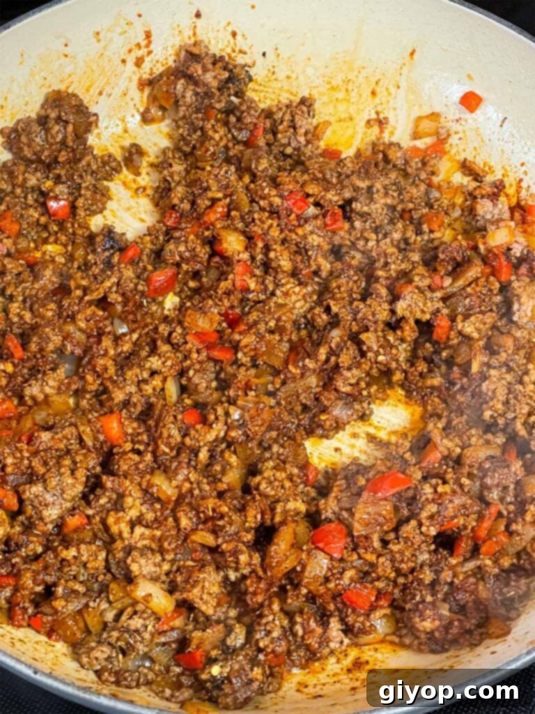The ground beef mixture in a skillet, with spices and tomato paste incorporated.