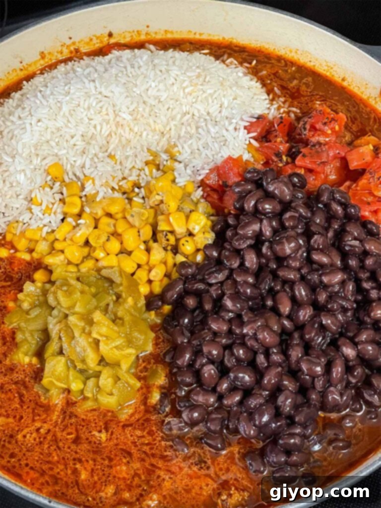 Multiple ingredients including broth, rice, beans, and corn being added to the Mexican ground beef mixture in a skillet.