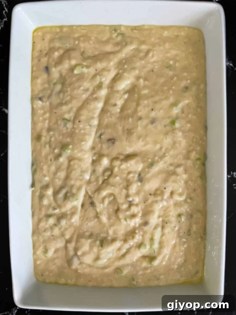 Soup and rice mixture for chicken and rice casserole in a light baking pan on a dark surface.