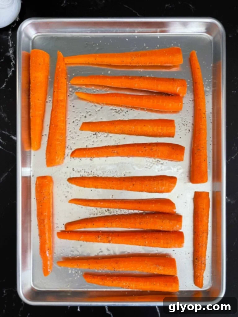 Raw whole carrots tossed in oil and seasonings on a metal rimmed baking sheet.