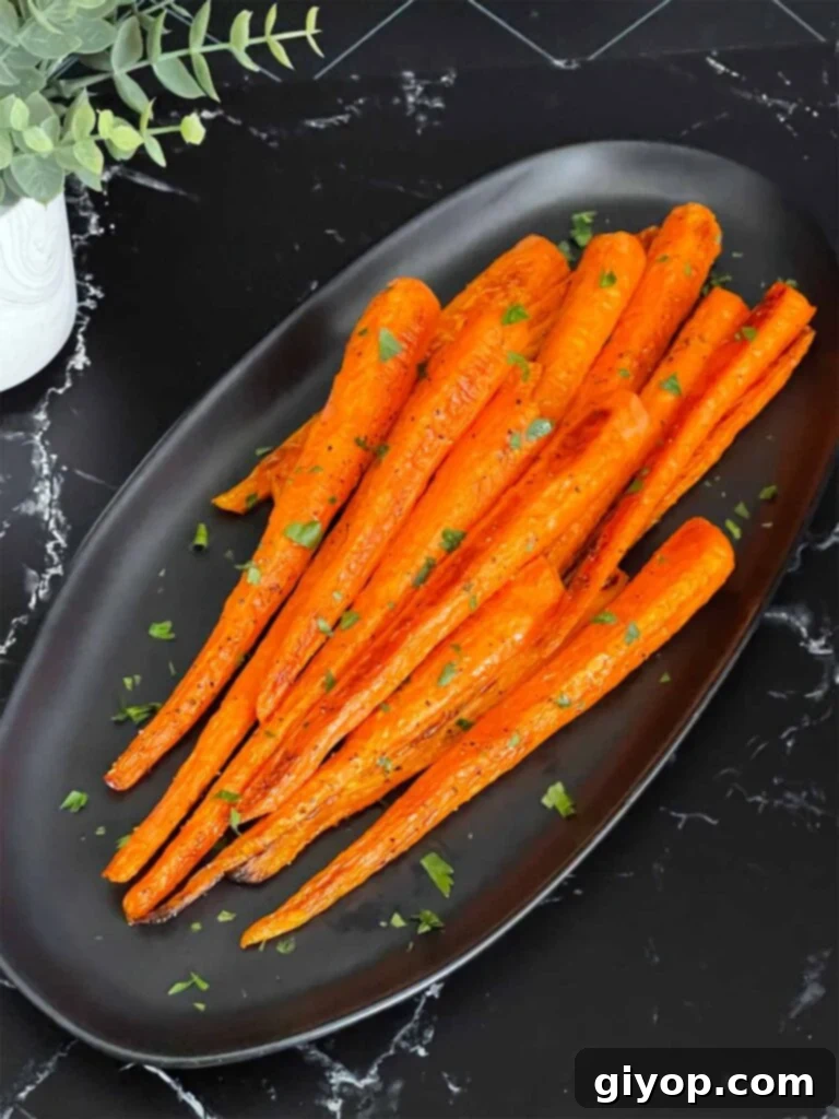 Roasted whole carrots on a dark plate garnished with chopped parsley.