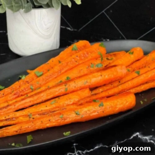 Roasted whole carrots on a dark plate garnished with chopped parsley.