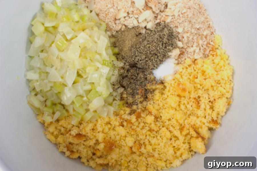Crumbled cornbread, sautéed celery and onions, dry breadcrumbs, and a selection of seasonings ready for mixing in a large bowl.