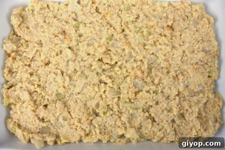 Unbaked southern cornbread dressing spread evenly in a white casserole dish, ready for the oven.