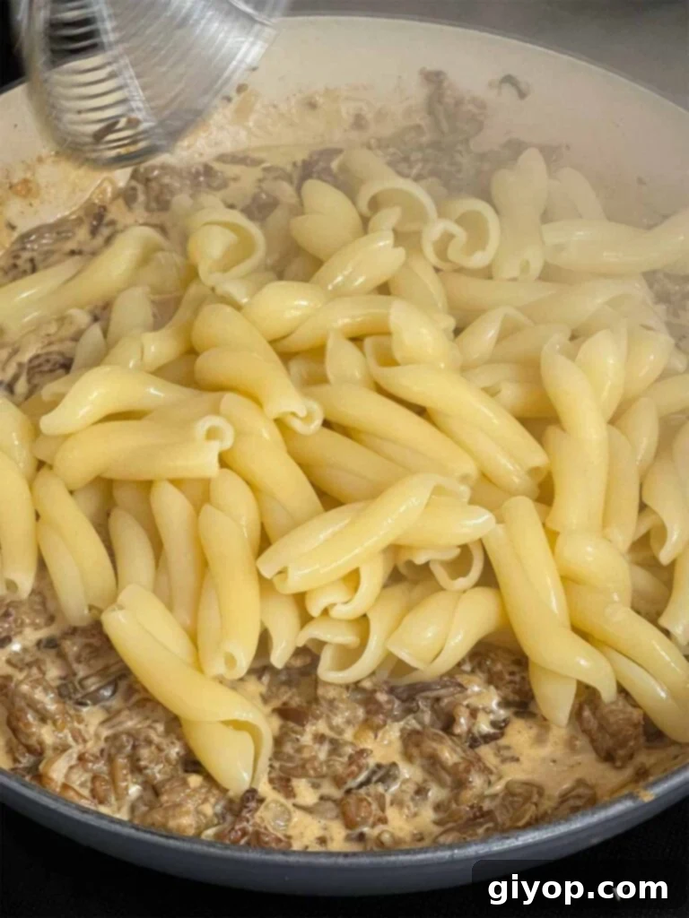 Adding pasta to a Pasta alla Norcina sauce in a skillet.