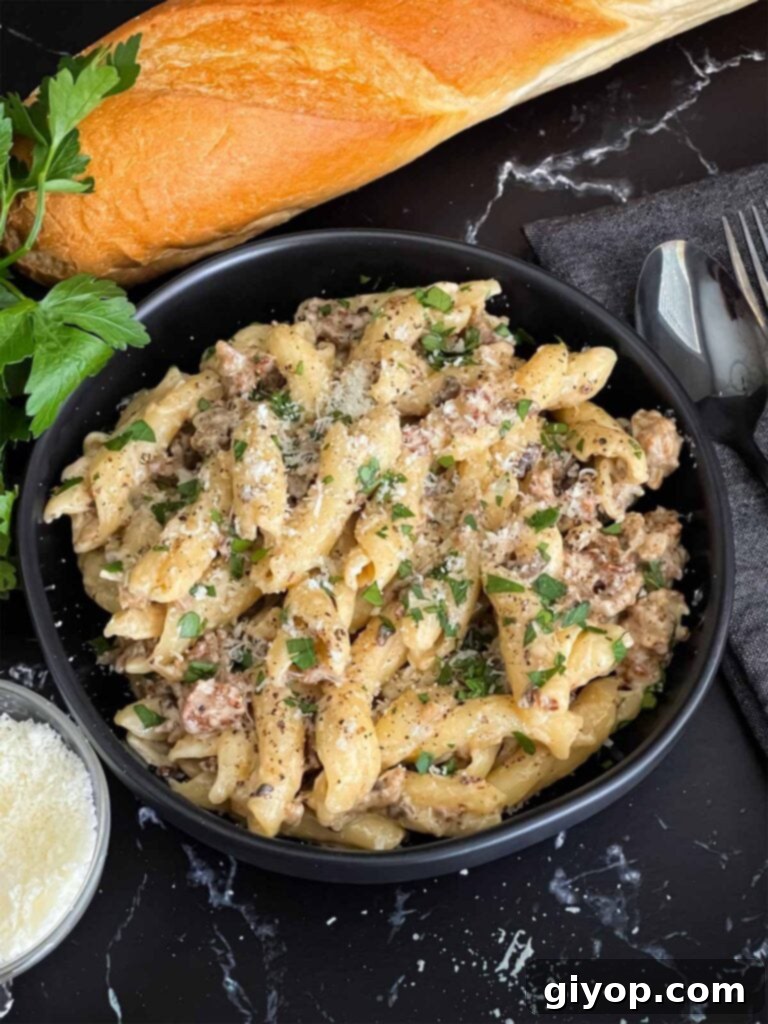 Pasta alla Norcina in a dark bowl with bread and parsley in the background.