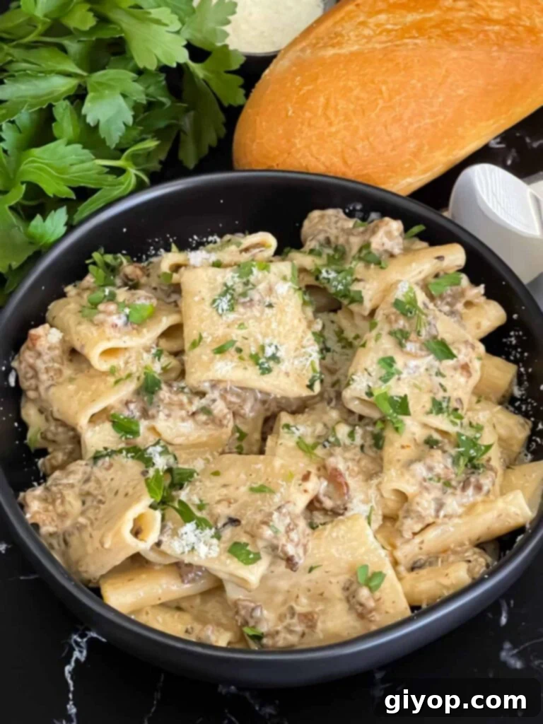 Pasta alla Norcina in a dark bowl with bread and parsley in the background.