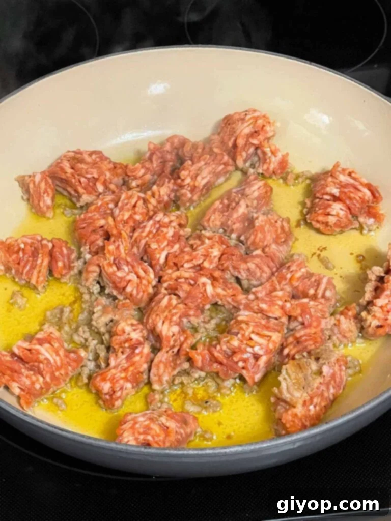 Broken up sausage in olive oil in a skillet.