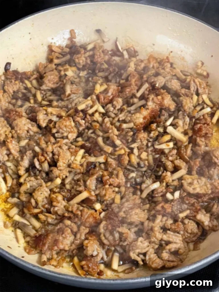 Browned Italian sausage and diced baby bella mushrooms cooking in a skillet.