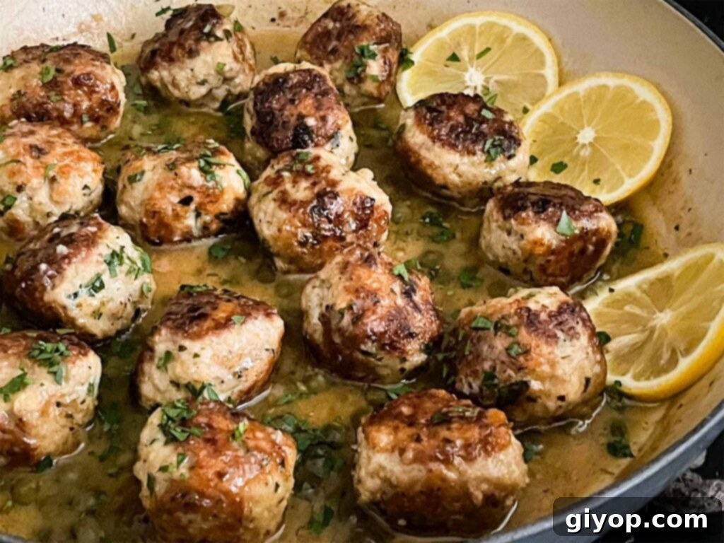 Savory Chicken Piccata Meatballs simmering in a rich lemon caper sauce in a large skillet.
