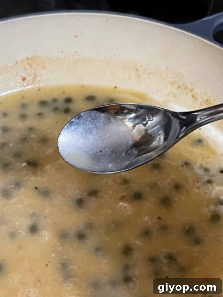 Close-up of the piccata sauce simmering in a skillet, showcasing its rich texture and bright components.