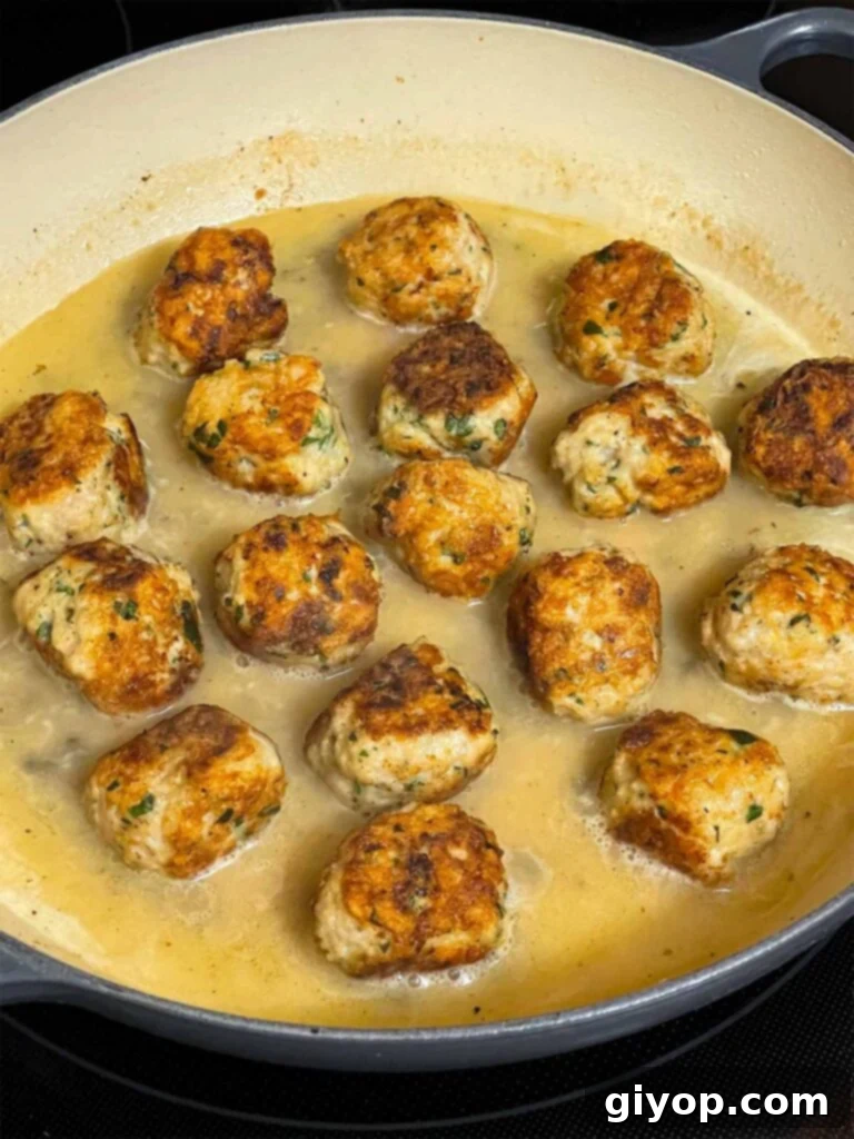 Fully cooked chicken piccata meatballs simmering in the glossy lemon caper sauce in a skillet.