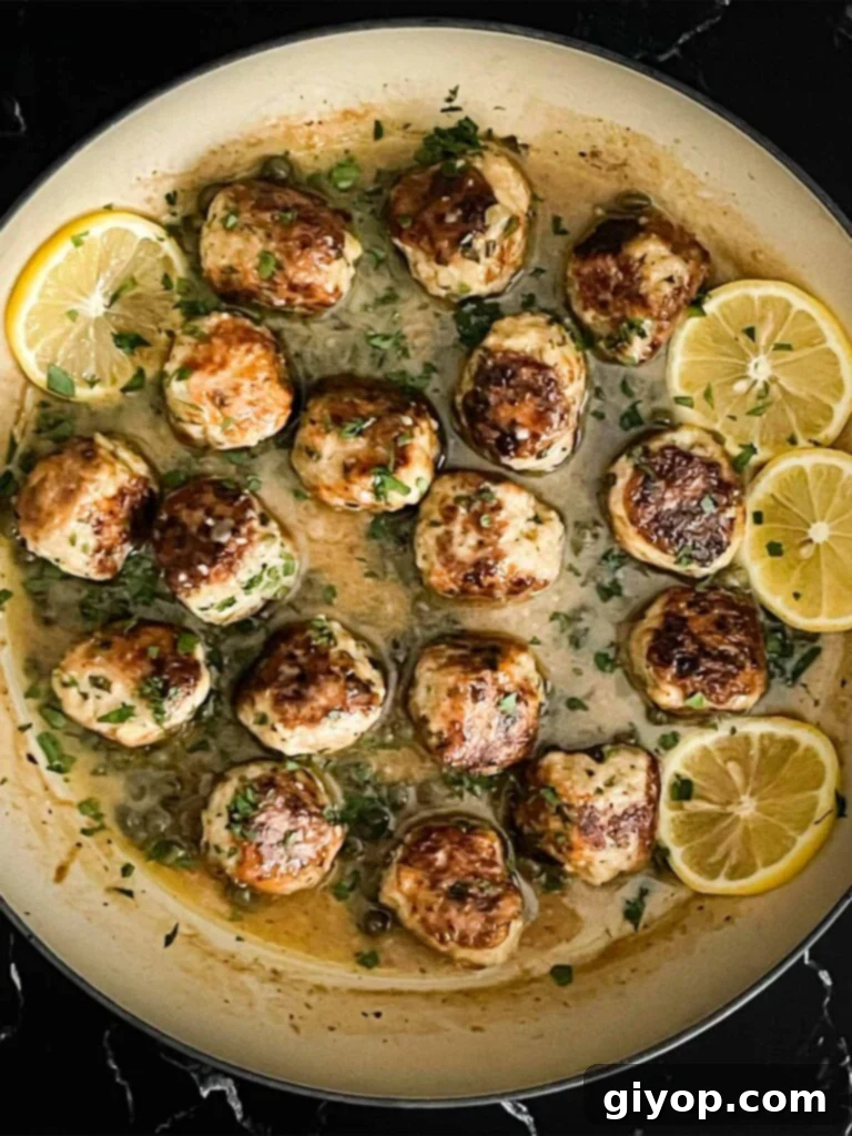 A close-up of chicken piccata meatballs in the skillet, garnished with fresh lemon slices and parsley.