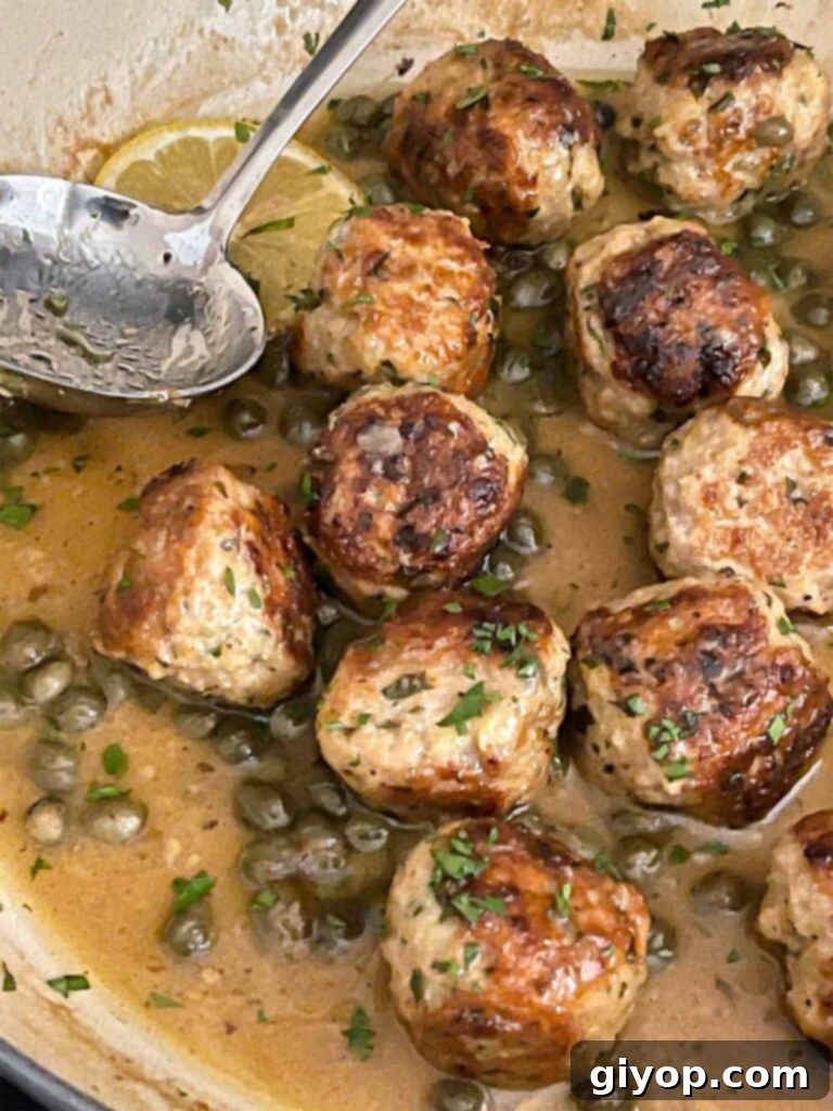 A wide shot of chicken piccata meatballs generously coated in sauce within a skillet, ready to be served.