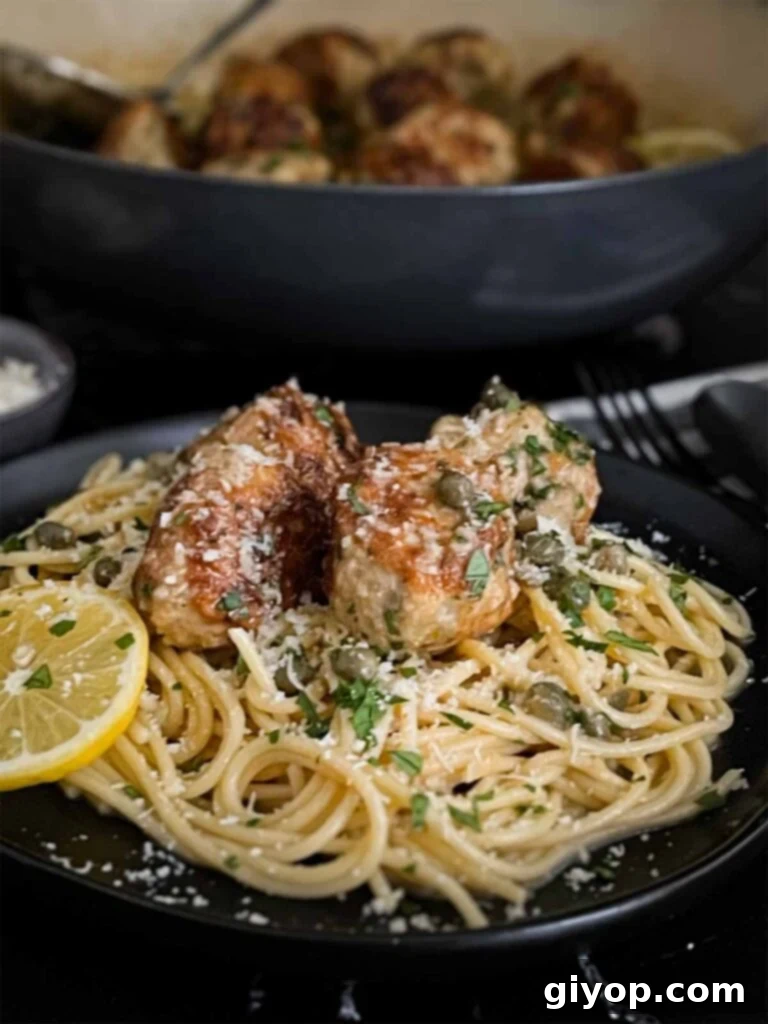 A serving of chicken piccata meatballs nestled on a bed of perfectly cooked pasta, coated in the flavorful sauce.