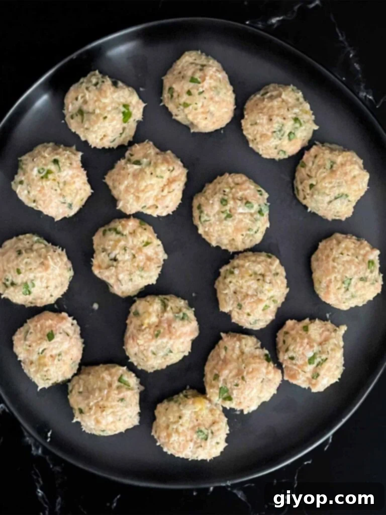 Neatly formed chicken piccata meatballs arranged on a dark plate, awaiting cooking.