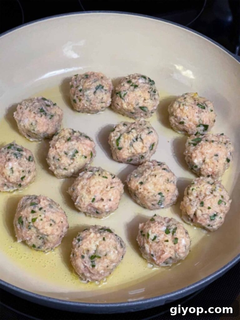 Golden-brown chicken piccata meatballs searing in a hot skillet with olive oil.