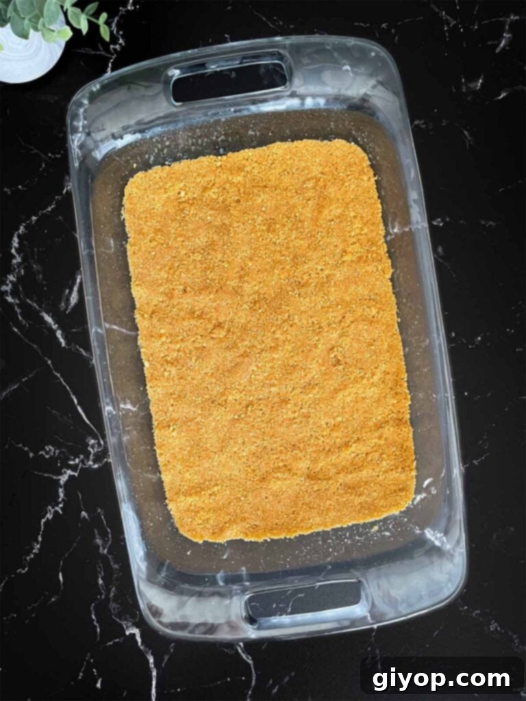 Velvet Coconut Dream 4 The graham cracker crust mixture expertly pressed into a 9x13 glass baking pan, ready for chilling, on a dark surface.