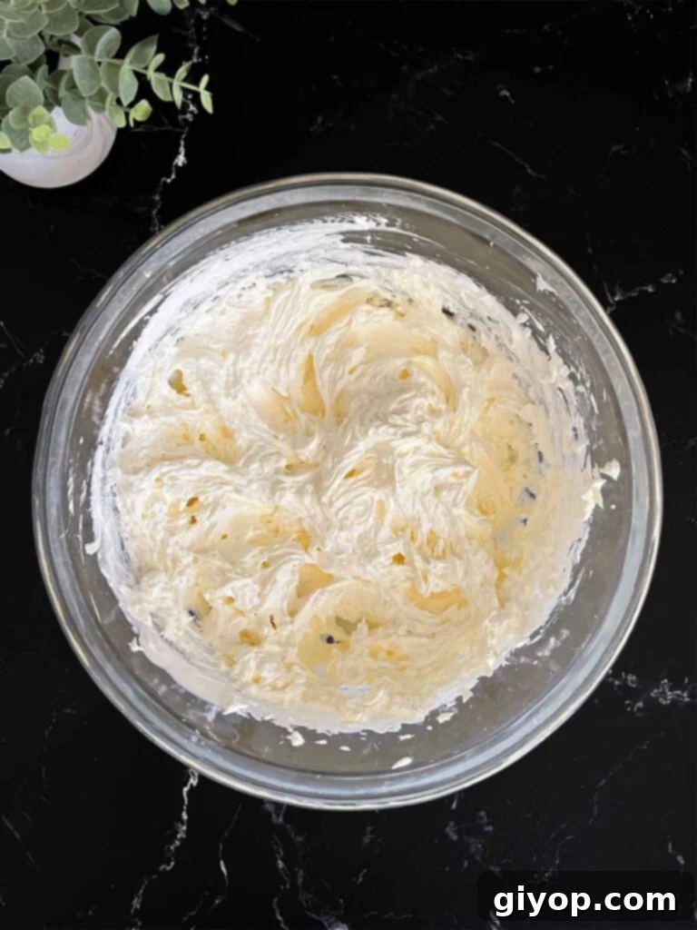 Velvet Coconut Dream 6 The process of gently folding whipped topping into the cream cheese and sugar mixture in a glass mixing bowl, creating a smooth blend, on a dark surface.
