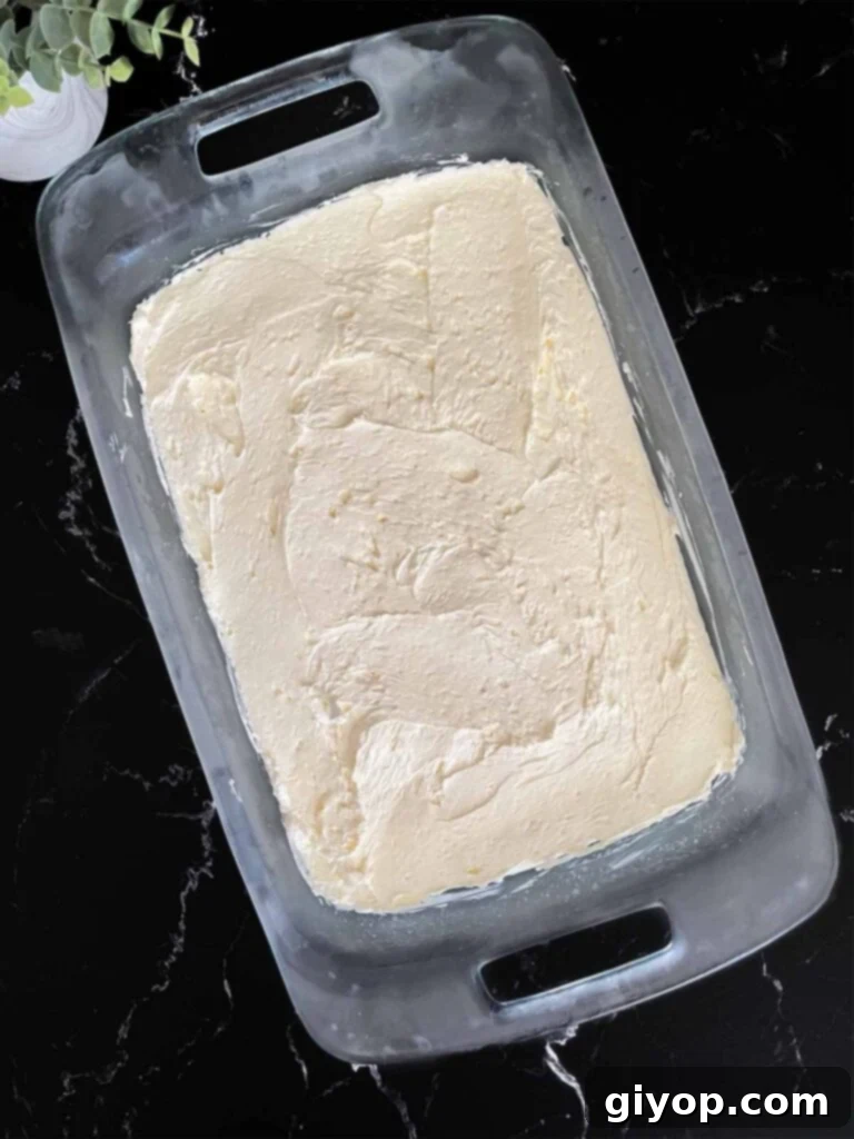 Velvet Coconut Dream 7 The smooth coconut cheesecake mixture spread meticulously over the graham cracker crust in a glass baking pan, ready for the next layer.