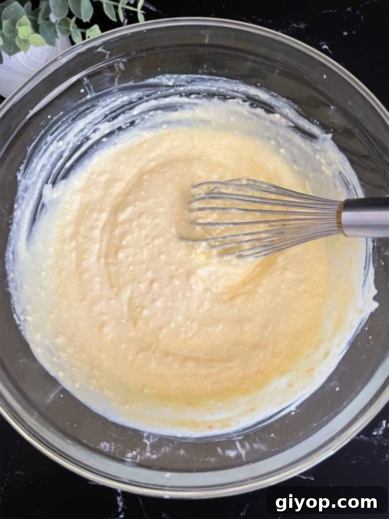 Velvet Coconut Dream 8 The coconut cream pudding mixture, now thick and creamy, thoroughly mixed with half and half in a glass mixing bowl, on a dark surface.