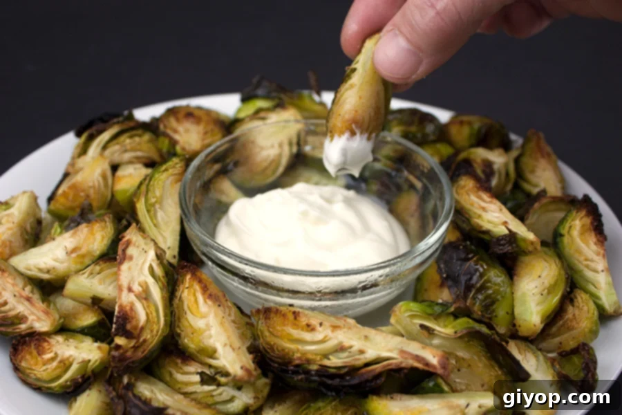 Roasted Brussel sprouts on a white plate with a glass ramekin of aioli, ready to be served.