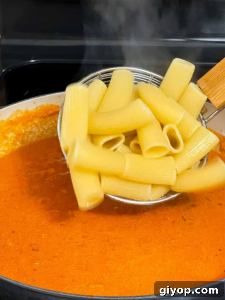 Adding cooked pasta to the vodka sauce in a skillet.