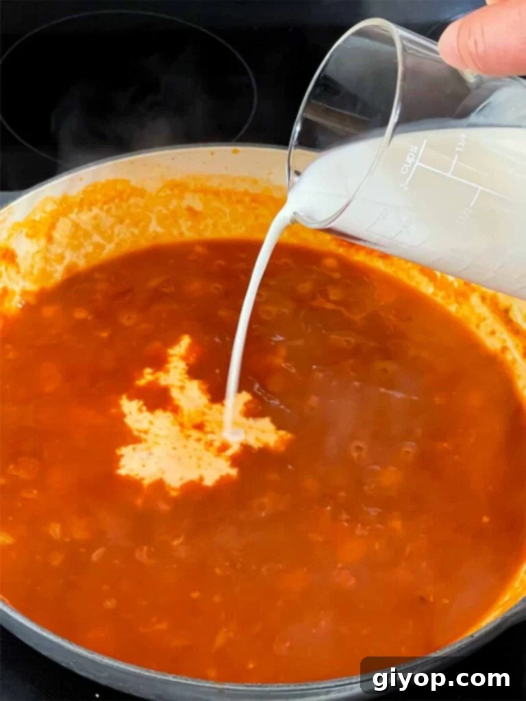 Adding cream to the simmering vodka sauce.