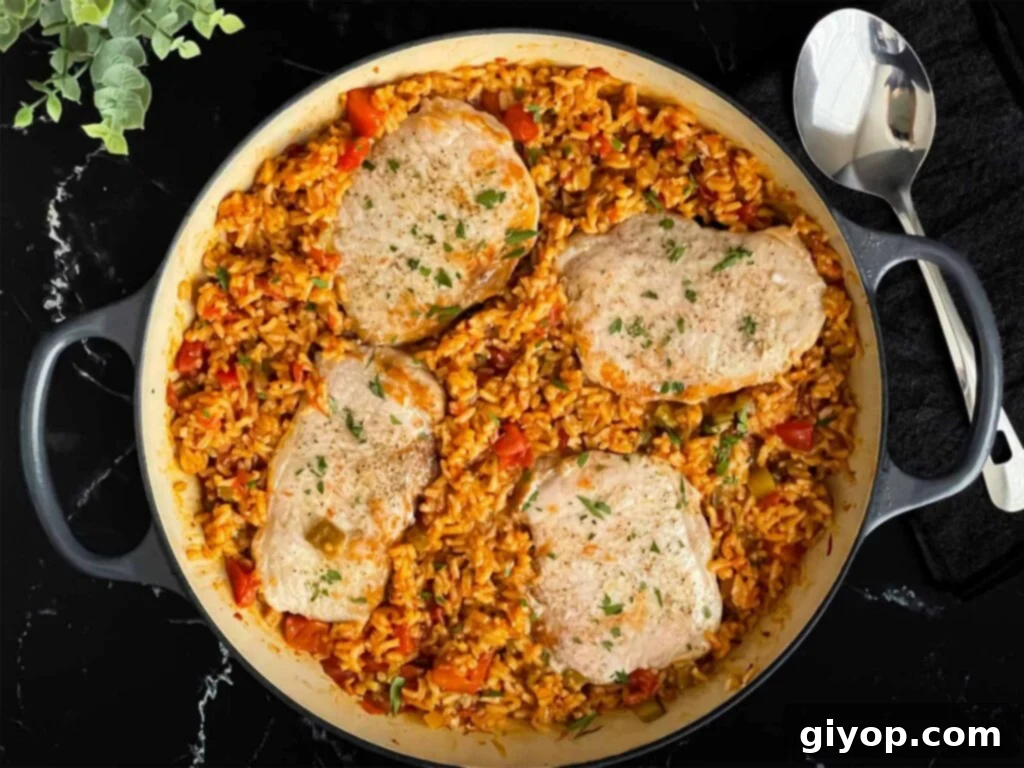 Spanish pork chops and rice garnished with chopped parsley in a light colored skillet.