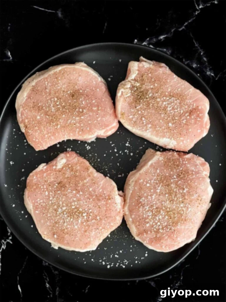 Boneless pork chops seasoned with kosher salt and black pepper on a dark plate.