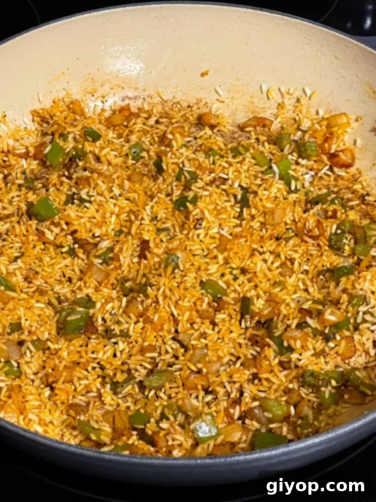 White rice, onions, green peppers, and seasonings tossed in a skillet for Spanish pork chops and rice recipe.