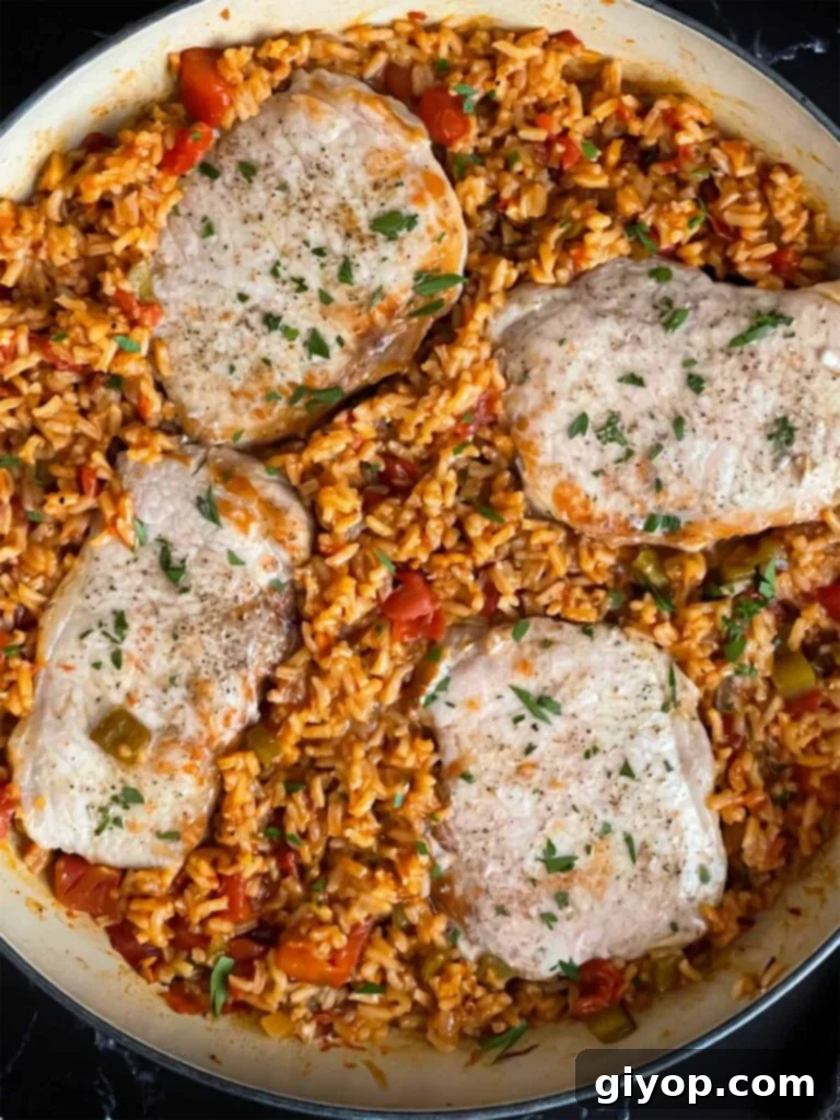 Spanish pork chops and rice garnished with chopped parsley in a light colored skillet.