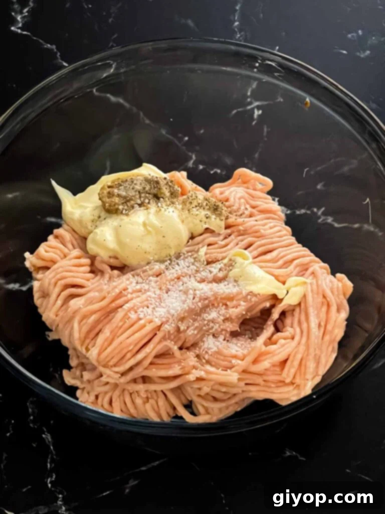 Ground chicken combined with mayonnaise, mustard, salt, and pepper in a glass bowl.
