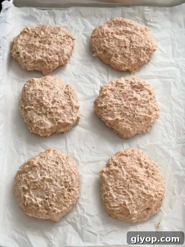 Six perfectly shaped raw chicken burger patties on parchment paper.