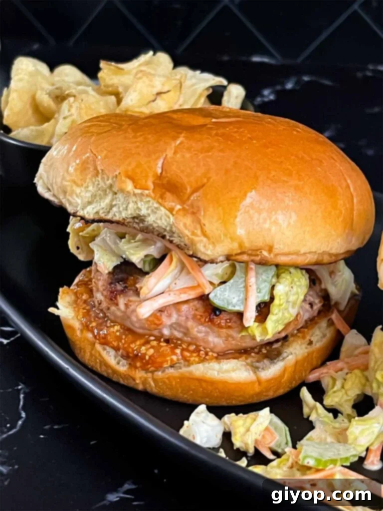 A fully assembled grilled chicken burger with Carolina barbecue sauce and ancho slaw, served on a black plate.